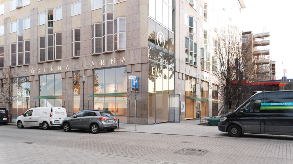 Bild som visar fasad och entré till Söderhallarna från Södermalms allé. Parkerade bilar vid gatan. Fotomontage